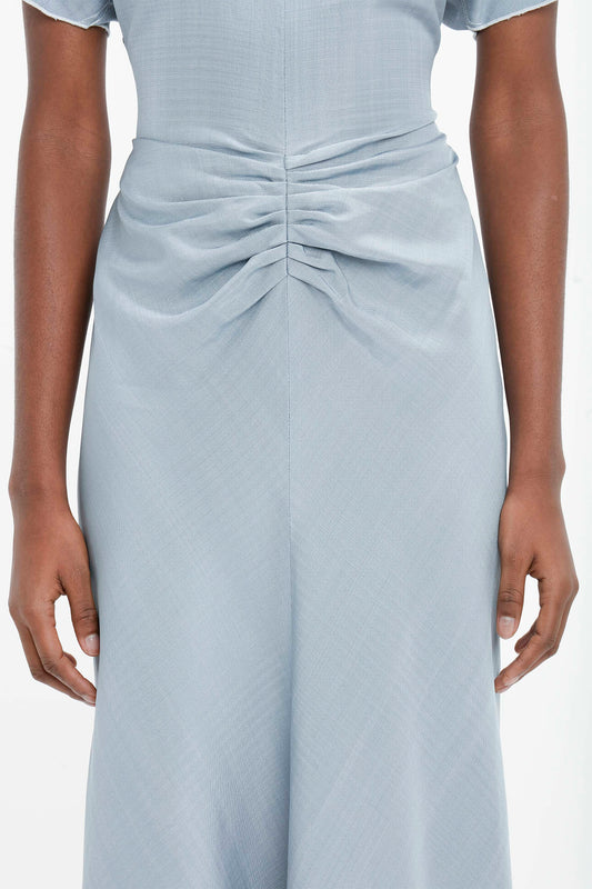 Close-up of the back of a light blue Exclusive Gathered Waist Midi Dress In Pebble, worn by a woman with her hands resting on her hips by Victoria Beckham.
