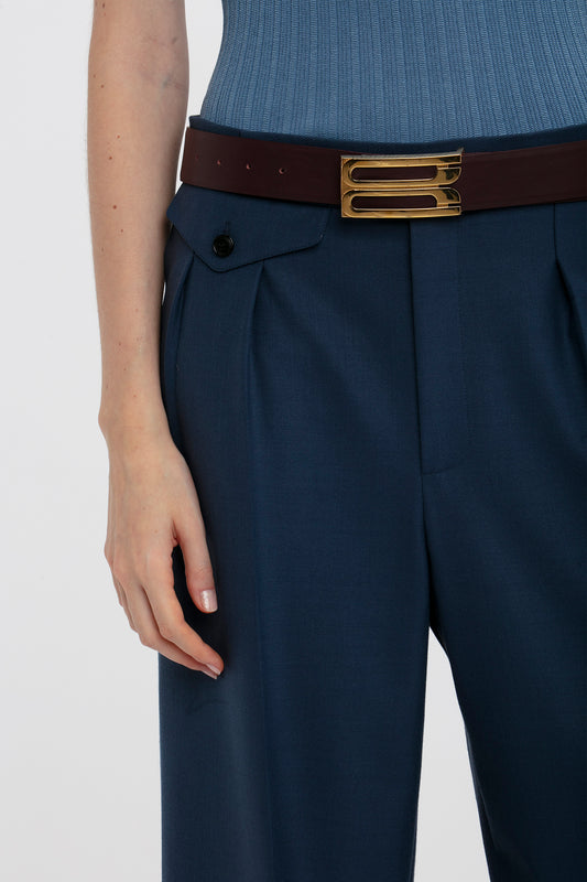 Close-up of a woman wearing Victoria Beckham high-waisted navy wide-leg cropped trousers with a brown belt and a tucked-in blue top, focusing on the belt and pocket detail.