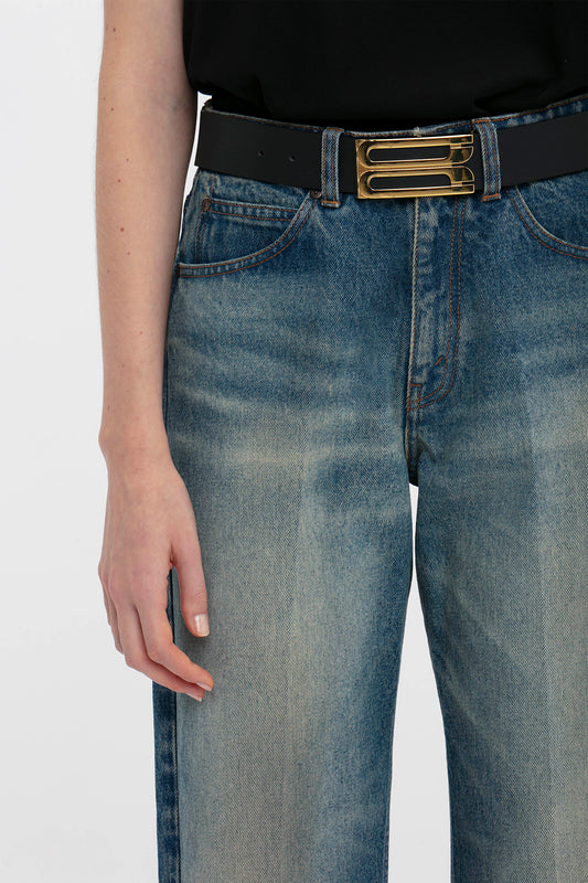 Close-up view of a person wearing Victoria Beckham relaxed straight leg jeans in antique indigo wash and a black belt with a gold buckle, focusing on the waist and upper thigh area.