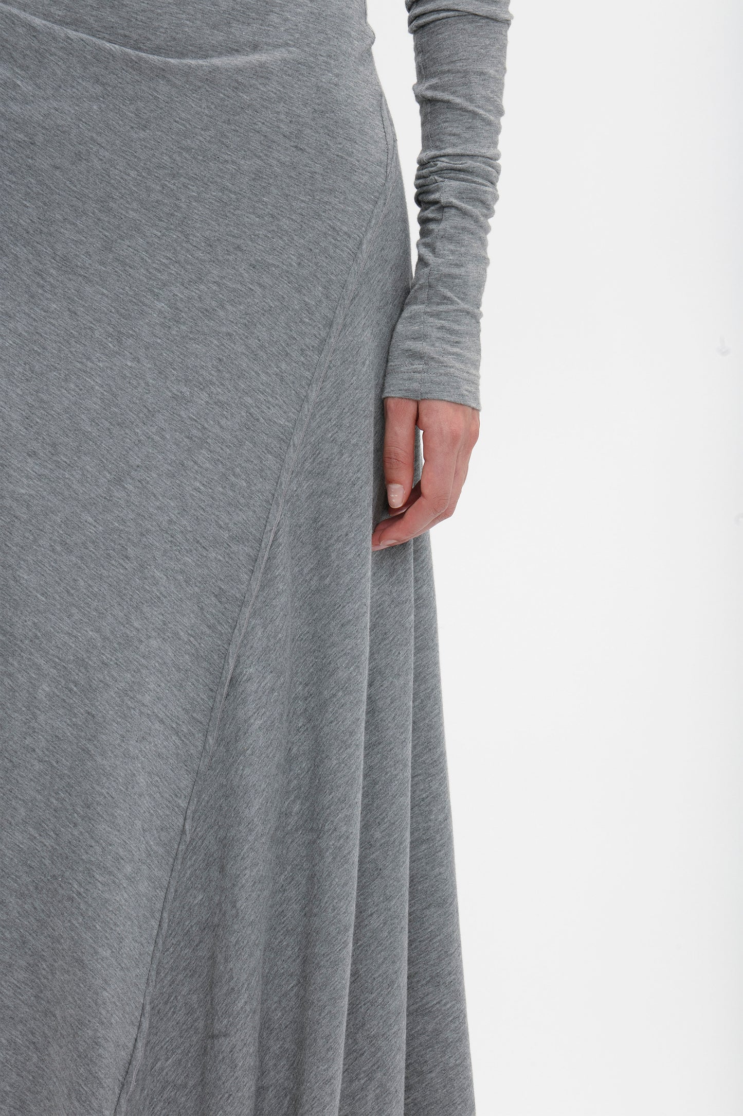 Close-up of a person wearing a Victoria Beckham Long Sleeve Circle Neck Dress In Grey Marl in super-soft cotton-jersey blend. The image shows the side of the dress and the person's hand touching the fabric, highlighting its contemporary eveningwear appeal.
