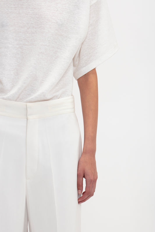 Close-up of a person wearing a white t-shirt and Victoria Beckham featherweight wool trousers, with a focus on the arm and hand resting lightly on the hip.