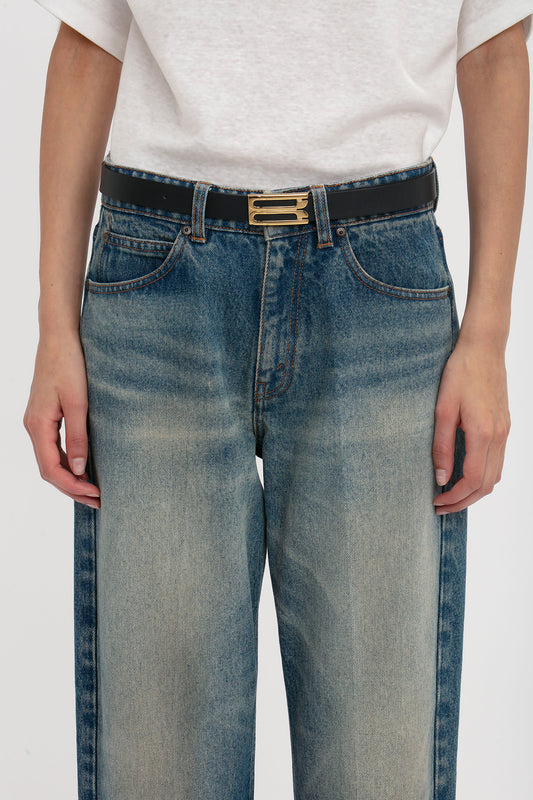 Close-up of a person wearing blue jeans and a white t-shirt, partially visible, with a Victoria Beckham Exclusive Frame Belt in Midnight Navy Leather featuring gold hardware.