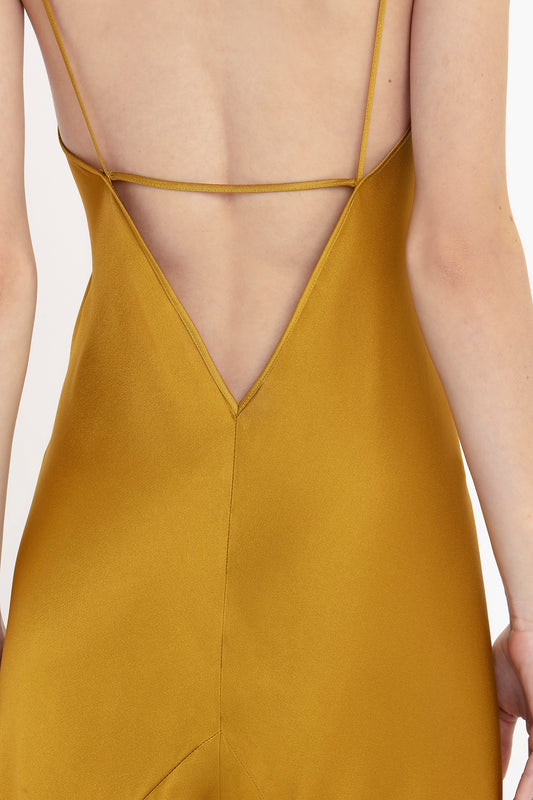 Rear view of a woman wearing a Victoria Beckham Low Back Cami Floor-Length Dress In Harvest Gold with thin crossed straps.