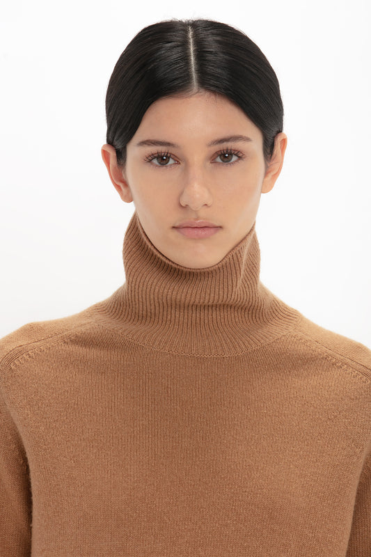 A woman with dark hair in a sleek style, wearing a Victoria Beckham luxury knitwear beige lambswool polo neck jumper in tobacco, looking directly at the camera with a neutral expression.