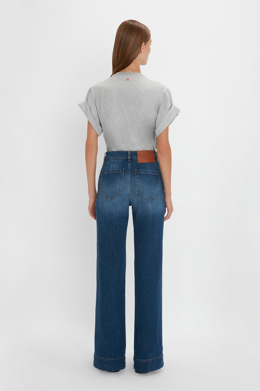 Rear view of a woman wearing Victoria Beckham's Alina Jean in Dark Vintage Wash and a gray t-shirt, standing in front of a white background.