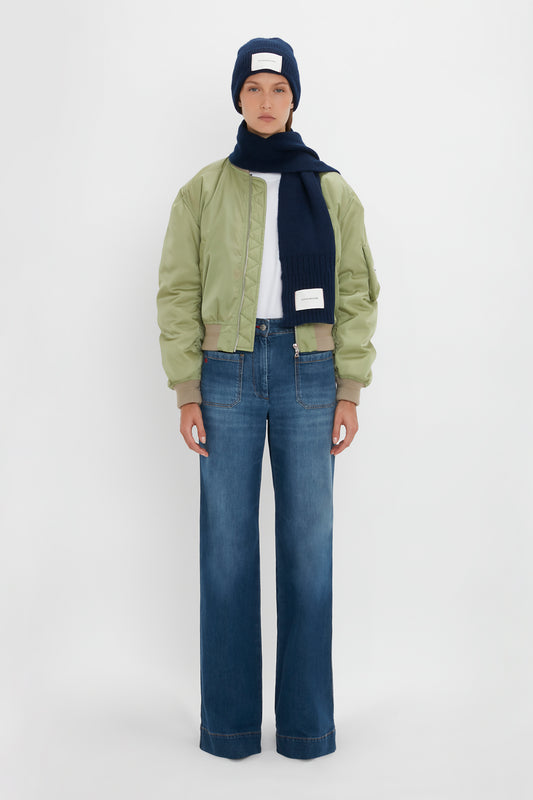A person in a green bomber jacket, blue logo patch beanie, and Exclusive Logo Patch Scarf In Navy from Victoria Beckham stands against a white background.