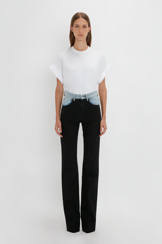 A woman stands against a white background wearing a white t-shirt and black relaxed leg jeans with a denim belt. The jeans are Victoria Beckham's Julia Jean In Contrast Wash.