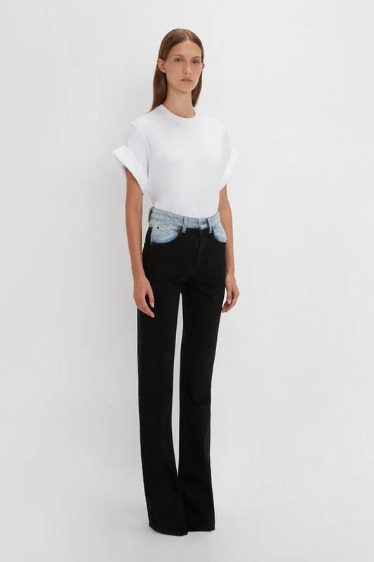 A woman in a plain white t-shirt and Victoria Beckham's Julia Jean In Contrast Wash high waist jeans with a denim belt stands against a white background.