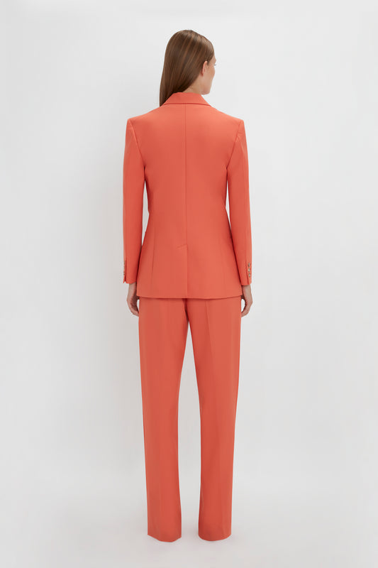 Woman standing with her back to the camera wearing a Victoria Beckham Patch Pocket Jacket In Papaya and straight-leg trousers against a white background.