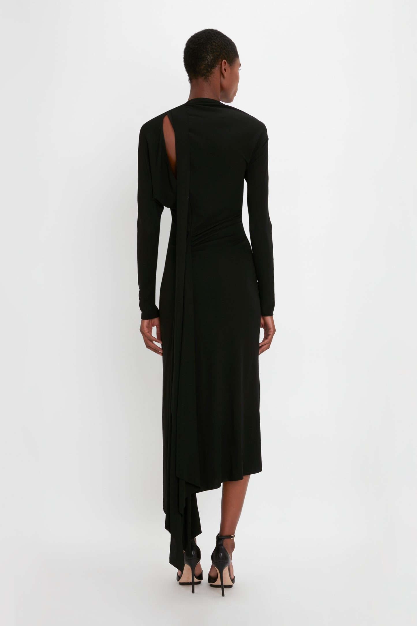 A woman in a Victoria Beckham Slash-Neck Ruched Midi Dress In Black with an asymmetric cut-out and twist details, posing on a plain white background.