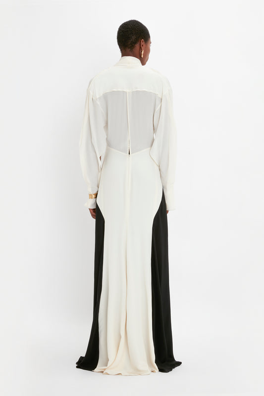 A person in a Victoria Beckham Tie Detail Gown In Vanilla-Black stands with their back to the camera against a plain background.