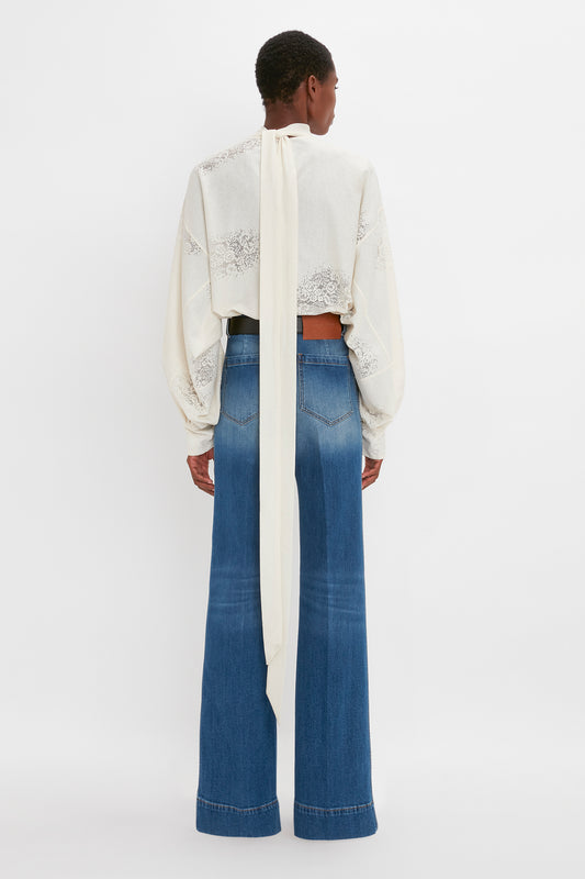 Woman seen from the back wearing a cropped, embellished Asymmetric Gather Detail Top in Cream with blouson sleeves and high-waisted blue jeans by Victoria Beckham.