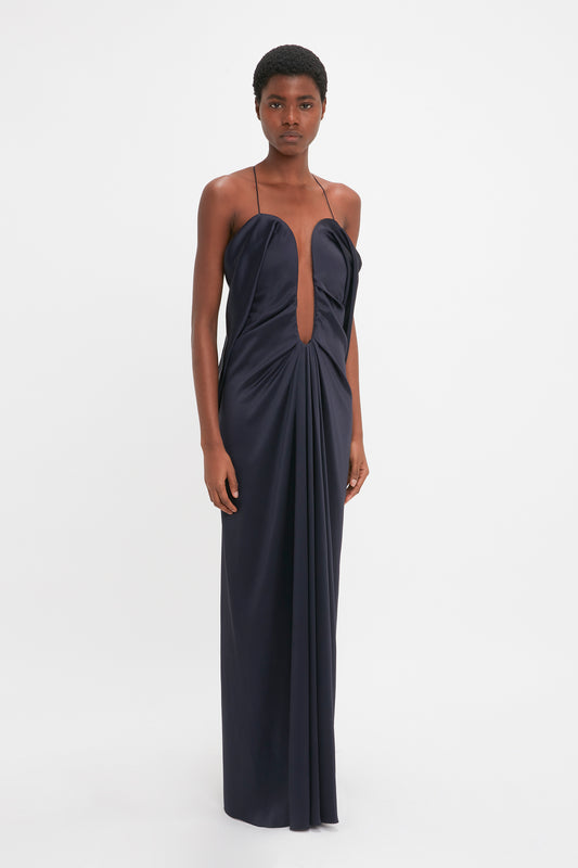 A black woman stands poised in a Victoria Beckham Frame Detail Cut-Out Cami Dress In Navy against a white background.