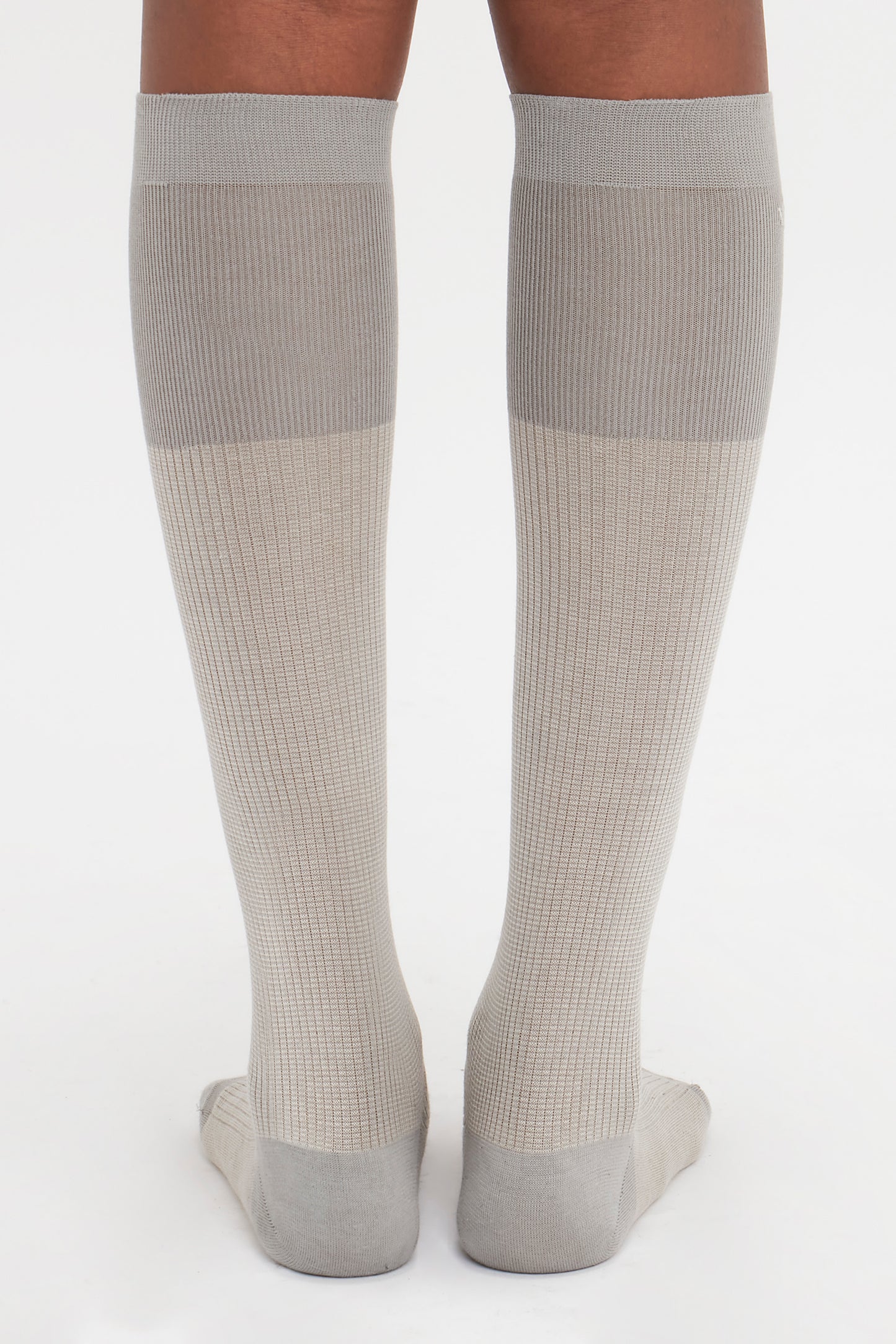 Back view of a person wearing knee-high, light gray Superfine Rib Socks In Lunar Grey by Victoria Beckham standing on a white background—an elevated wardrobe essential in 100% cotton.