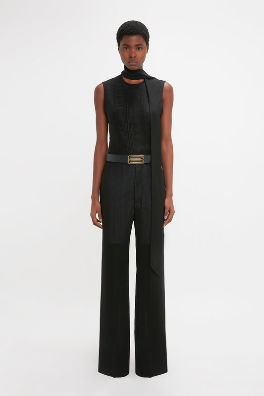 A black woman stands facing the camera, wearing a modern Victoria Beckham sleeveless top and high-waisted, Waistband Detail Straight Leg Trouser In Black with a belt.