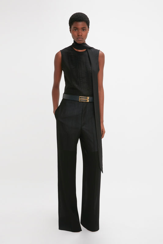 A black woman in a stylish sleeveless black jumpsuit with Victoria Beckham's Waistband Detail Straight Leg Trouser In Black, standing against a plain white background.