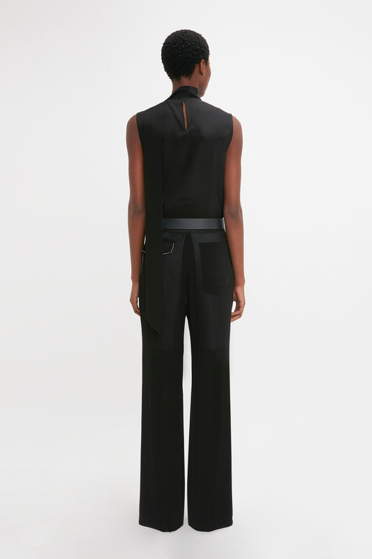 Woman from behind wearing Victoria Beckham's Waistband Detail Straight Leg Trouser In Black and a tailored black sleeveless top, standing against a white background.