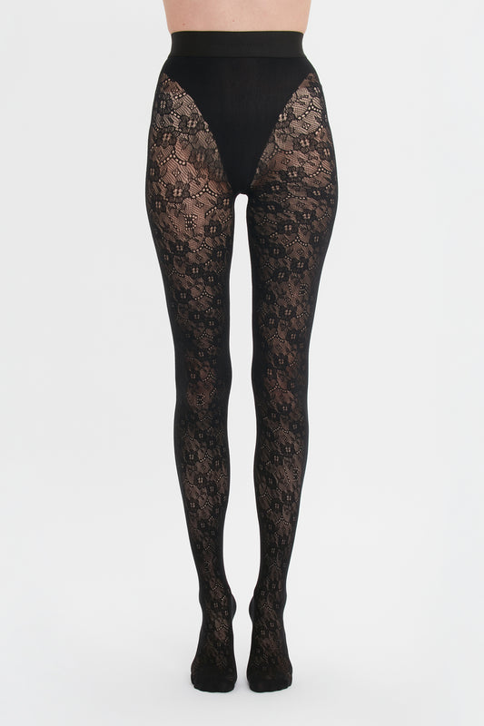 A person wearing decorative Victoria Beckham Exclusive VB Monogram Lace Tights In Black against a white background.