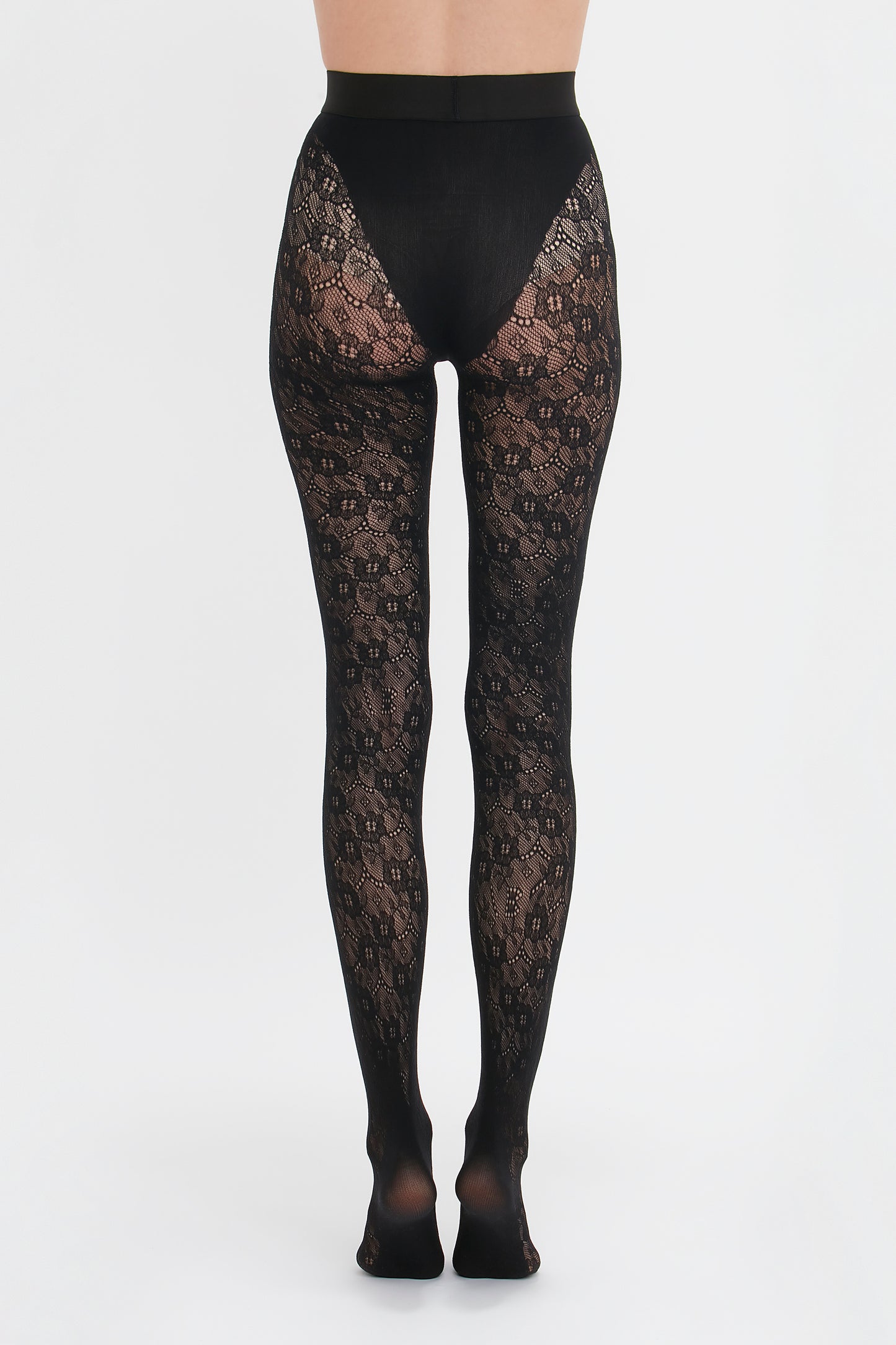 A person wearing black, intricate lace-patterned Victoria Beckham Monogram Lace Tights against a white background.