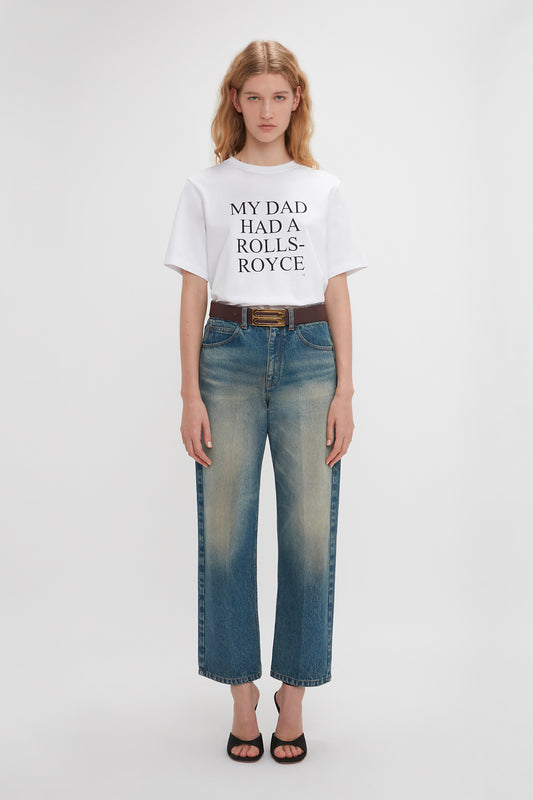 Woman in a white Victoria Beckham exclusive 'My Dad Had A Rolls-Royce' slogan T-shirt and blue jeans, standing against a plain background.