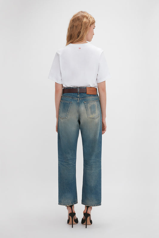 Woman in a Victoria Beckham Exclusive 'My Dad Had A Rolls-Royce' Slogan T-shirt in white and blue jeans standing facing away, highlighting the back design and fit of the clothing.
