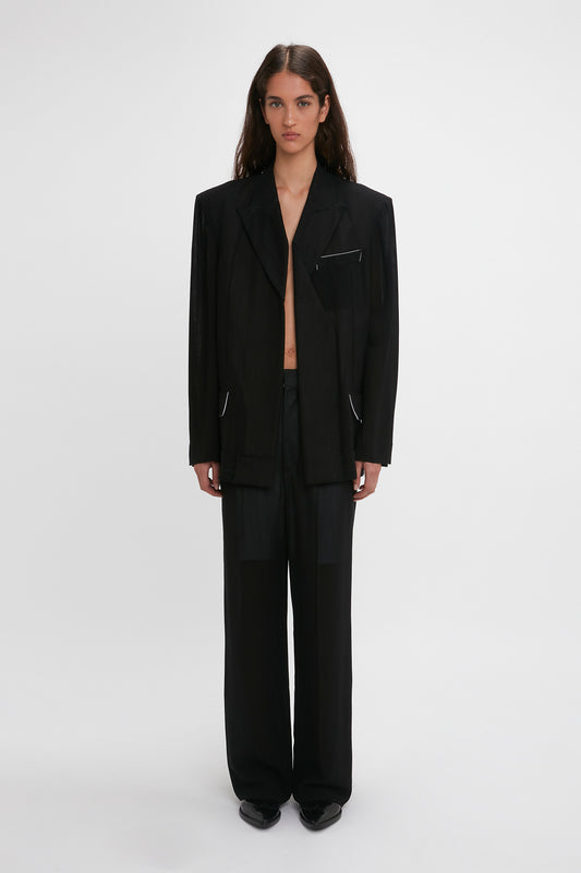 A woman in a Victoria Beckham Fold Detail Tailored Jacket In Black with an unbuttoned front stands against a white background, looking directly at the camera.