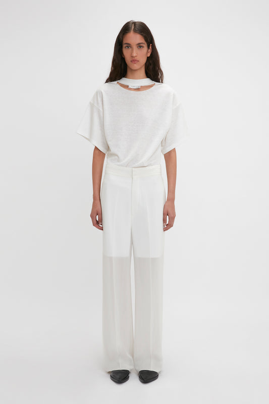 A woman stands against a white background, wearing a white oversized t-shirt and high-waisted, wide-leg featherweight wool pants with black shoes by Victoria Beckham.