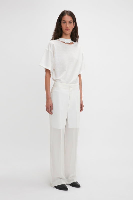 A woman stands against a white background wearing a white draped top and Waistband Detail Straight Leg Trousers in featherweight wool, paired with black flat shoes by Victoria Beckham.