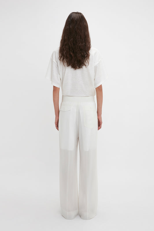 Woman in a white t-shirt and Victoria Beckham Waistband Detail Straight Leg Trousers standing against a plain background, viewed from the back.