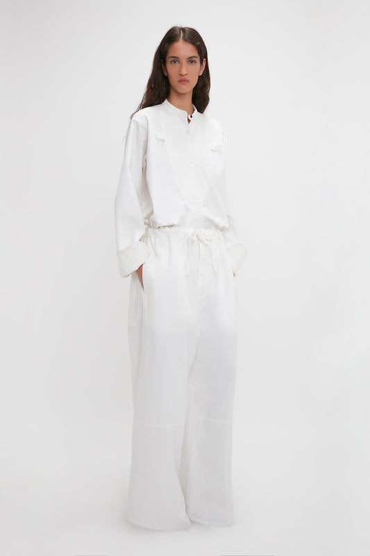 A woman wearing a white button-up shirt and cotton-canvas Victoria Beckham drawstring pyjama trousers in washed white, standing against a plain white background.