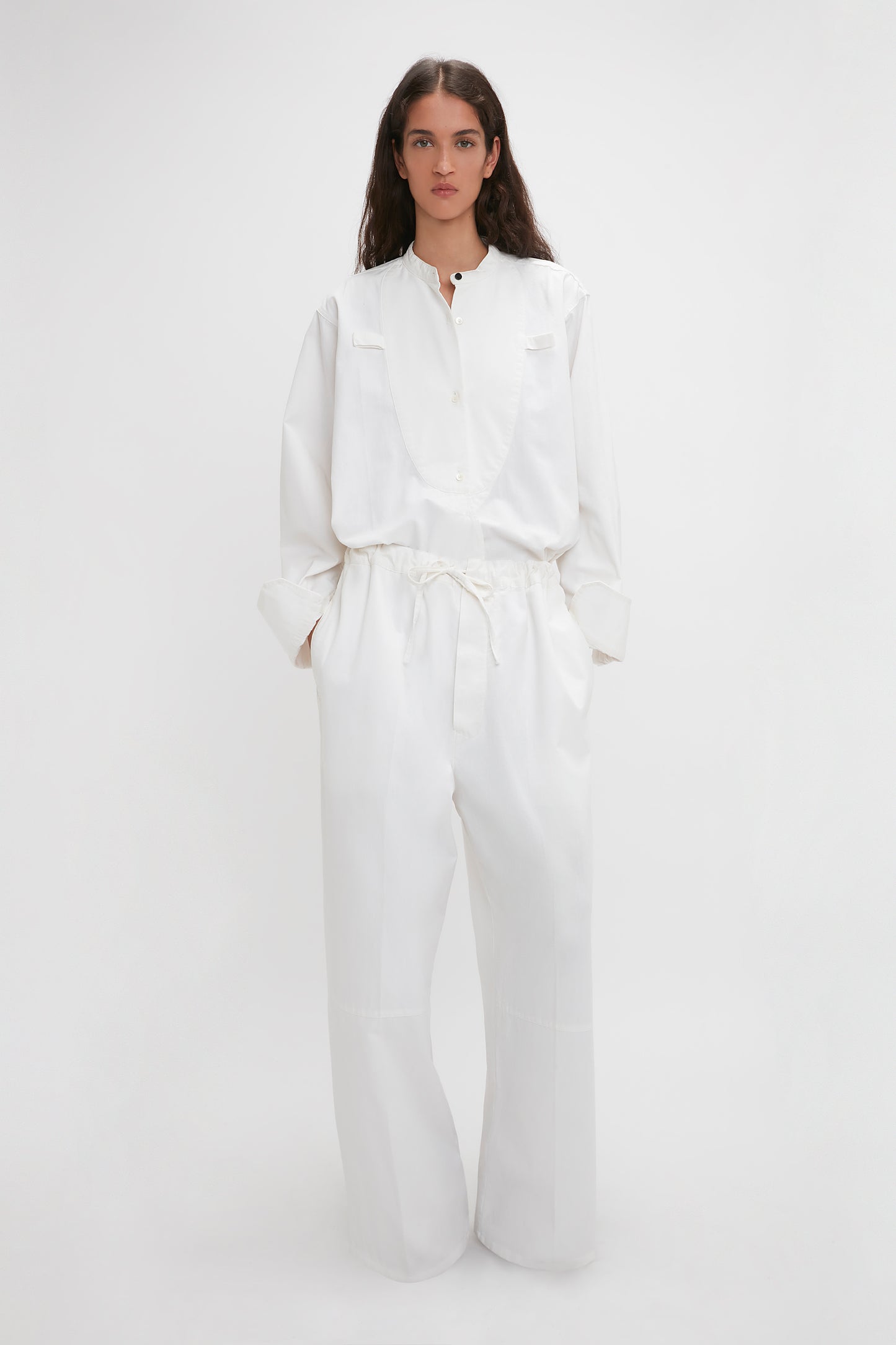 Woman wearing Victoria Beckham's Drawstring Pyjama Trouser In Washed White with cuffed sleeves and high-waisted, wide-leg trousers, standing against a plain background.