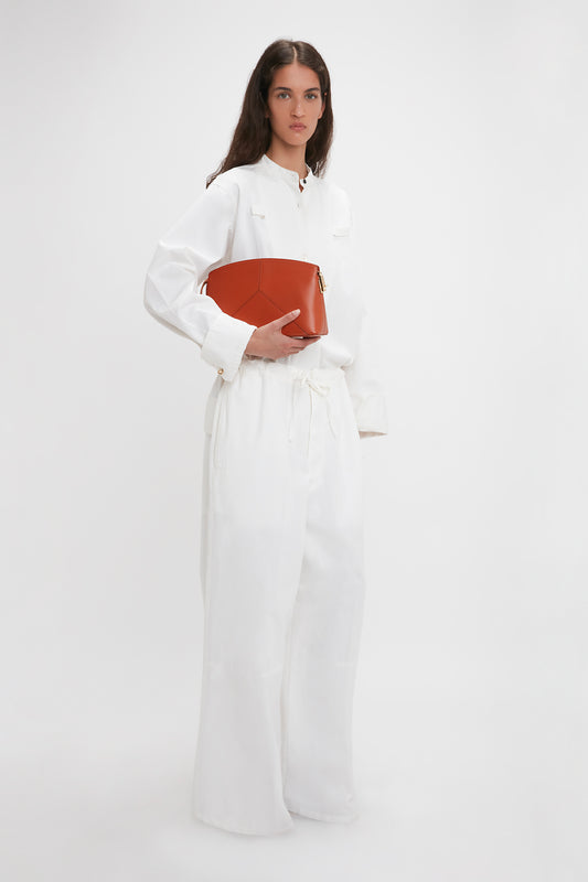 A woman in Victoria Beckham's washed white drawstring pyjama trousers holds a red handbag, standing against a plain white background.
