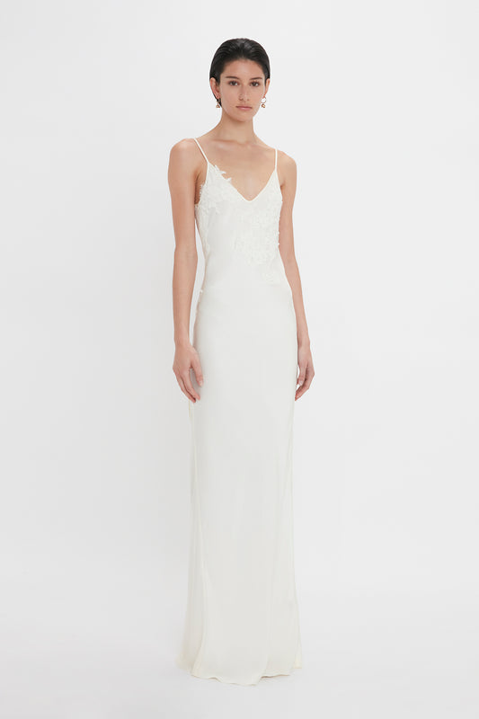 A woman in a white sleeveless lace-top wedding gown and Victoria Beckham's Exclusive Camellia Flower Hoop Earrings In Gold standing against a plain white backdrop.