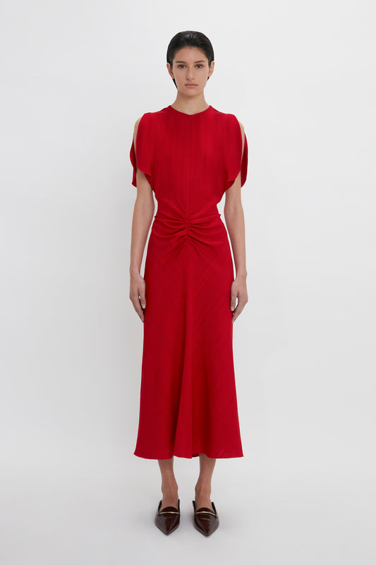 Woman in a red Victoria Beckham Exclusive Gathered V-Neck Midi Dress In Carmine with a twisted front detail, standing against a white background.