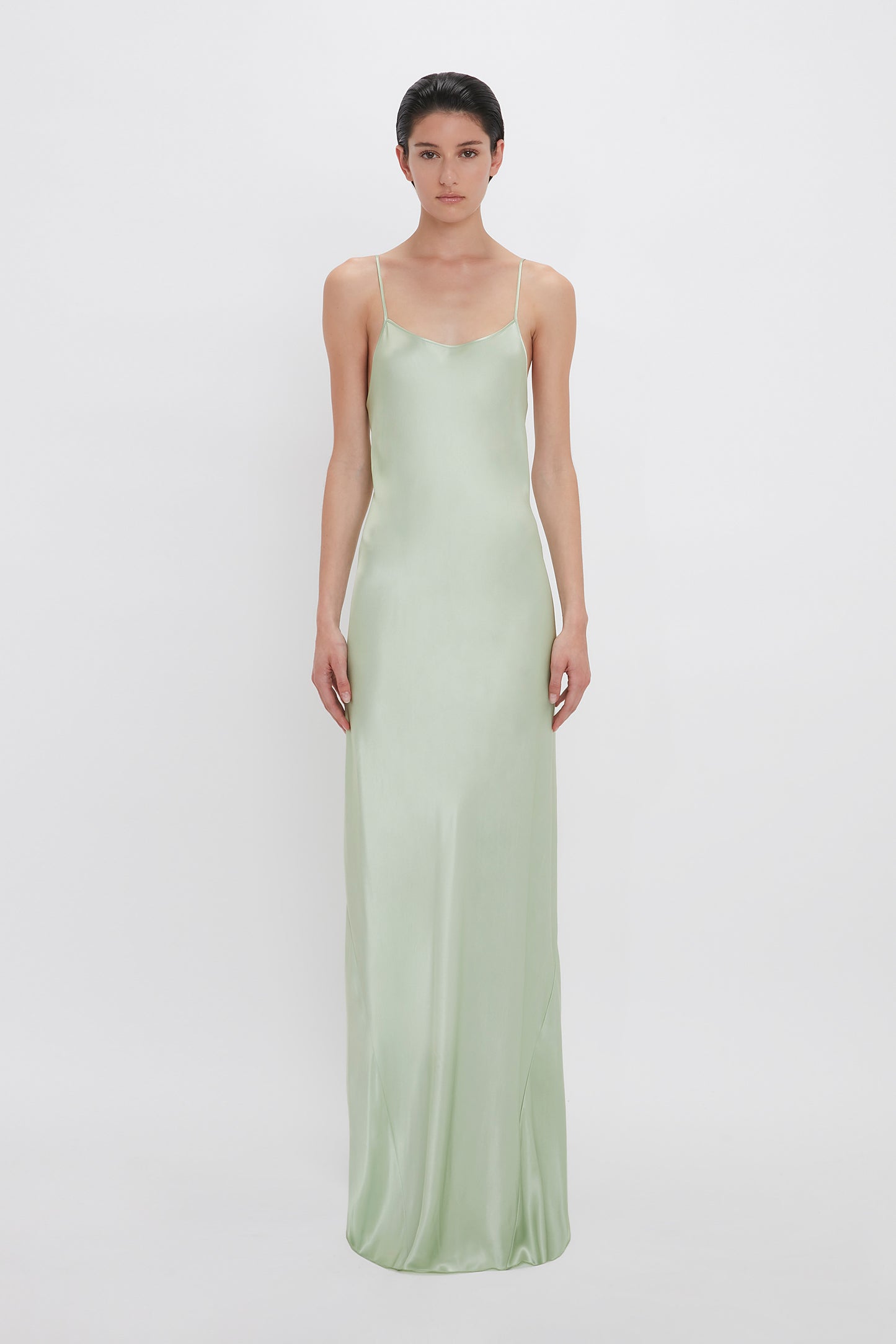 A woman in a Victoria Beckham Exclusive Low Back Cami Floor-Length Dress In Jade stands against a white background, looking directly at the camera.