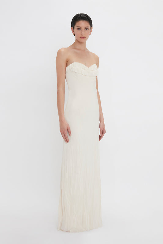 A woman in a sleek, white strapless sweetheart neckline Victoria Beckham gown stands against a plain white background, looking directly at the camera.