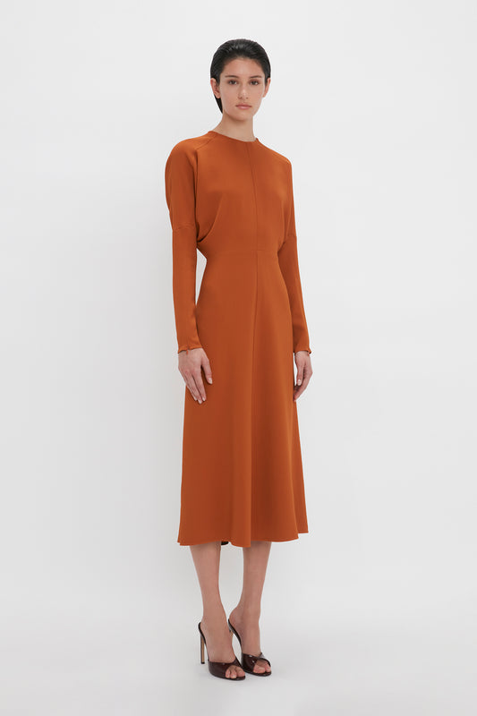 Woman in a tailored, long-sleeve Victoria Beckham Dolman Midi Dress in Russet standing against a white background.
