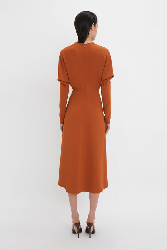 A woman in a sleek russet Victoria Beckham Dolman Midi Dress and black high heels, viewed from behind against a plain white background.