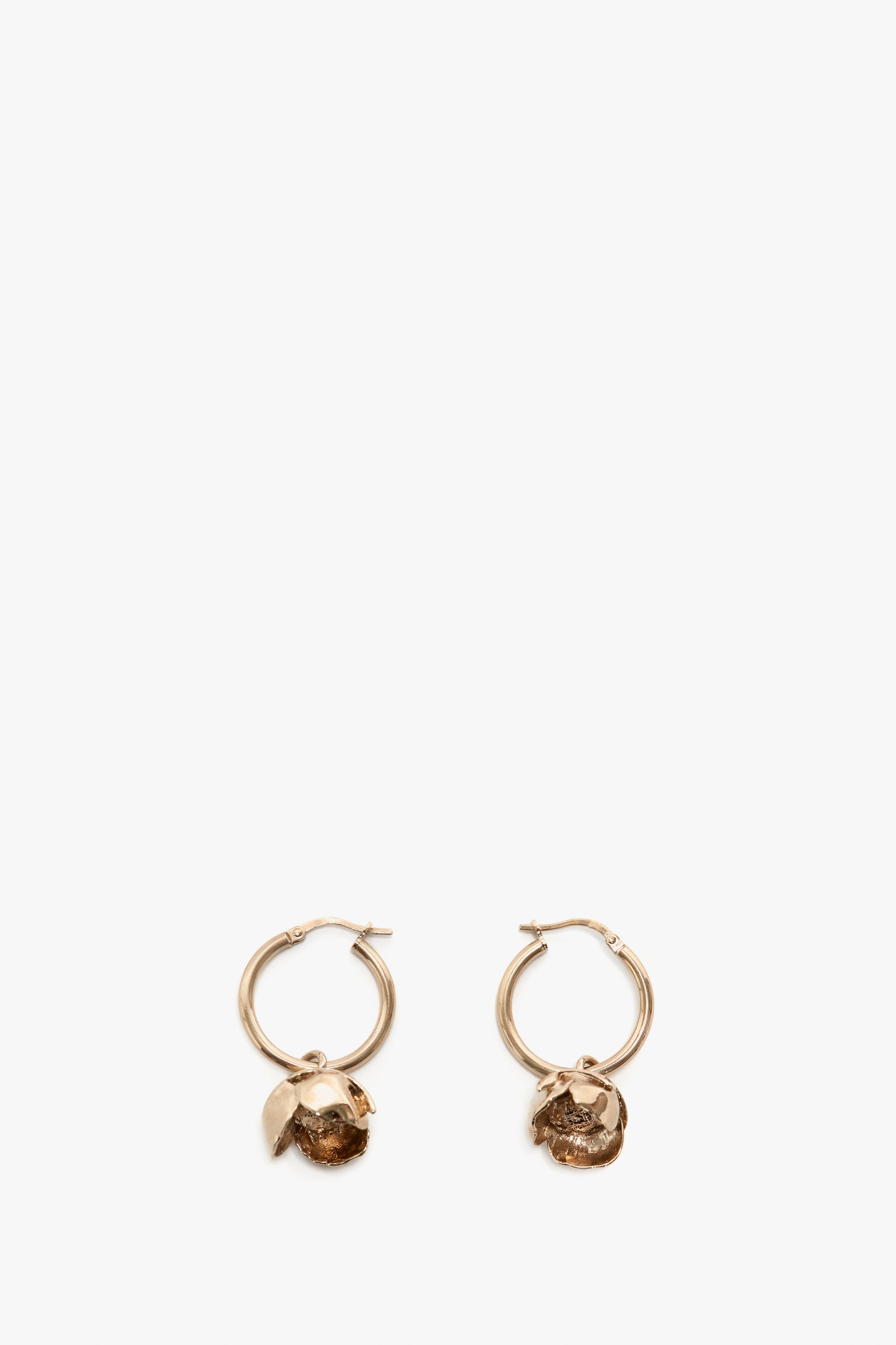 A pair of Exclusive Camellia Flower Hoop Earrings In Gold by Victoria Beckham with small decorative lion heads, isolated on a white background.
