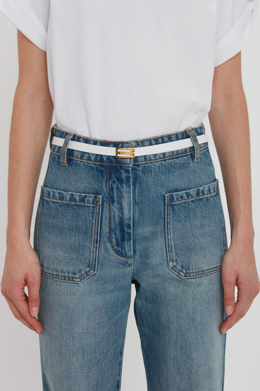 Close-up of a person wearing blue jeans with a Victoria Beckham Exclusive Micro Frame Belt in White Leather, focusing on the waist and back pockets.