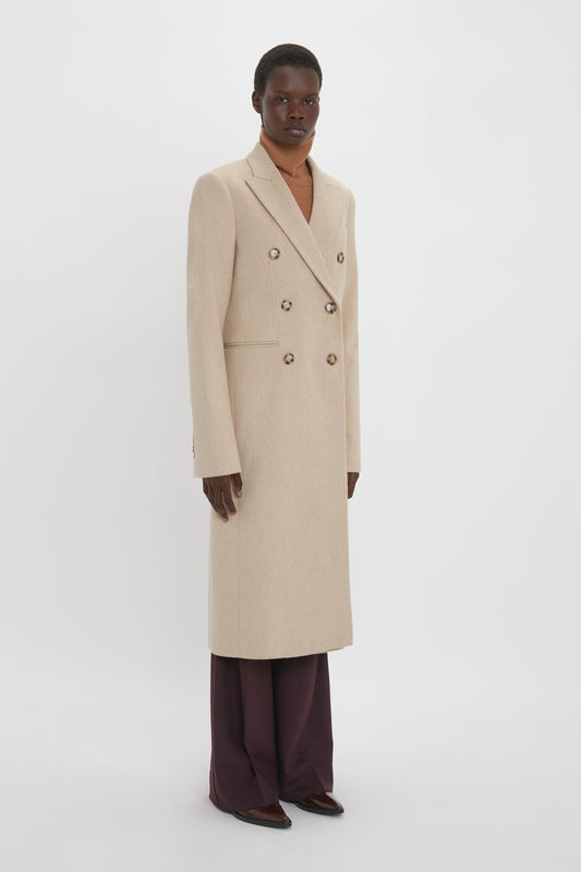 A tall black man wearing a Victoria Beckham Tailored Slim Coat In Bone over dark burgundy pants, standing against a white background.