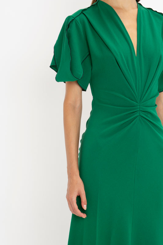 Close-up of a woman wearing a green Victoria Beckham Gathered V-Neck Midi Dress in Emerald with ruffled sleeves and a twisted detail at the torso.