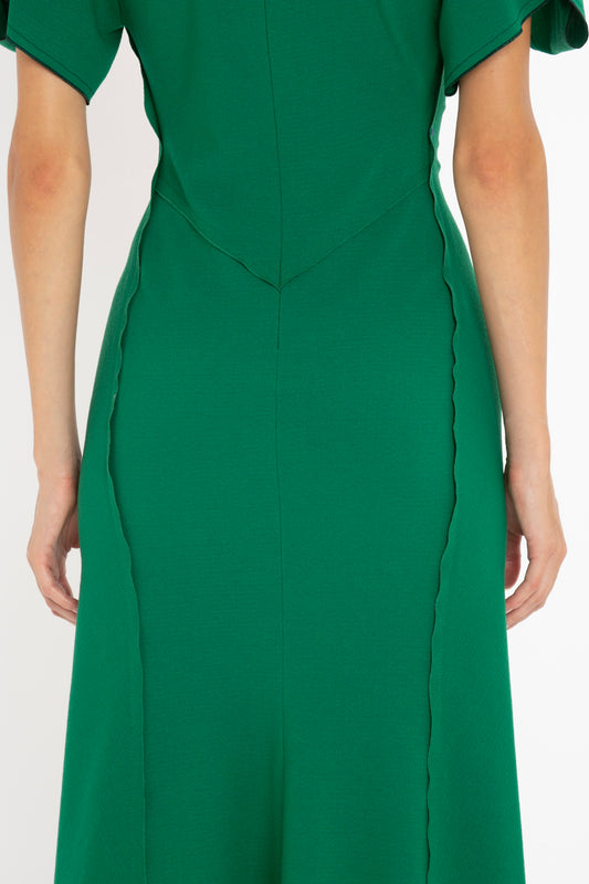 Close-up of a woman wearing a Victoria Beckham Gathered V-Neck Midi Dress in Emerald with short sleeves and scalloped trim detailing. The focus is on the torso area.