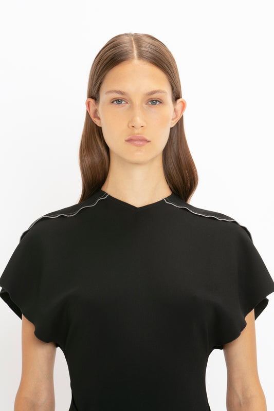 Portrait of a woman with straight brown hair and a Short Sleeve Tie Detail Dress In Black by Victoria Beckham, featuring a scalloped neckline and front-tie detail, against a white background.