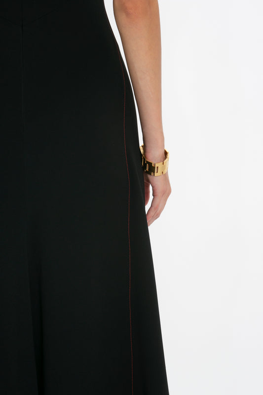 Side view of a woman wearing a Victoria Beckham black dress with front-tie detail, focusing on her wrist wearing a gold watch.