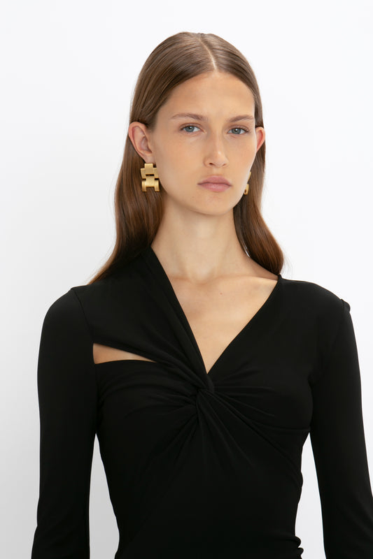 Woman in a Victoria Beckham Tie Detail Floor-Length Dress in Black and gold link earrings, posing against a white background.