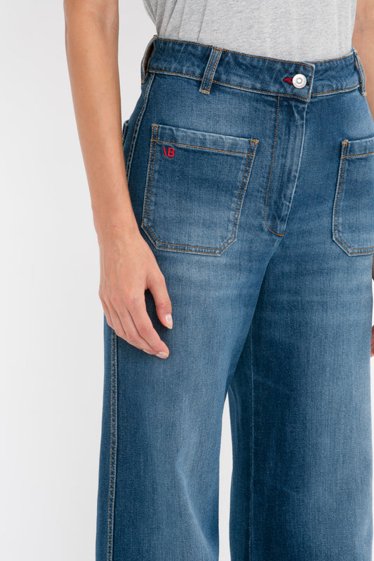 Close-up of a person wearing Alina Jean in Dark Vintage Wash by Victoria Beckham with a hand resting lightly on the hip, showcasing the jeans' back pocket with a red Victoria Beckham logo.