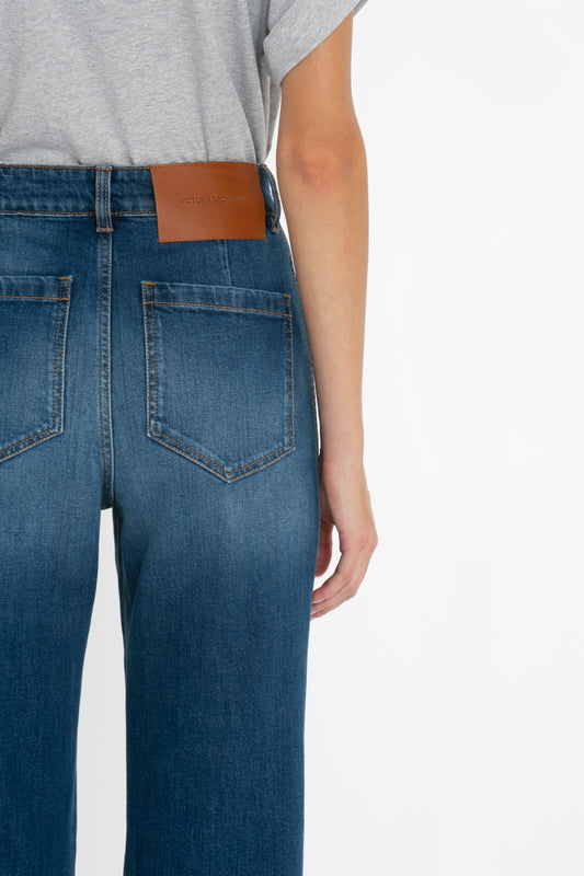 Close-up of a person wearing Alina Jeans in Dark Vintage Wash with a brown leather patch on the back right pocket labeled "Victoria Beckham.