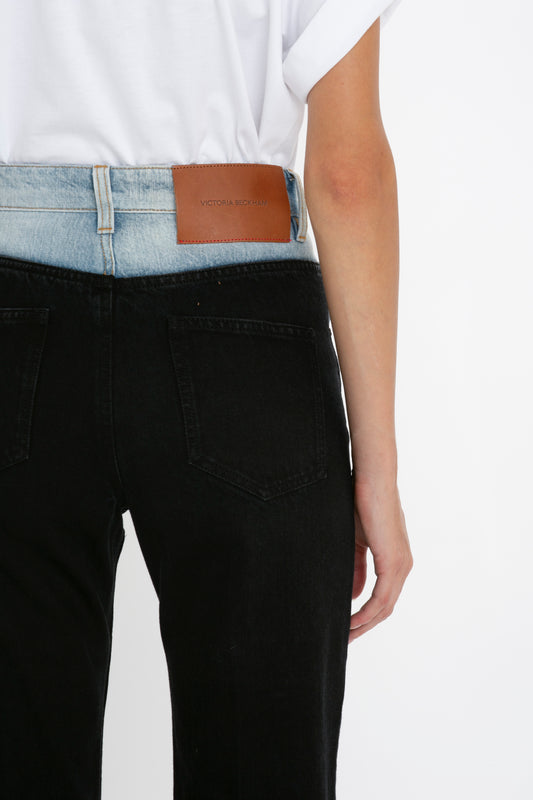 Rear view of a person wearing black relaxed leg jeans with a Victoria Beckham Julia Jean In Contrast Wash label on the waistband, paired with a tucked-in white t-shirt.