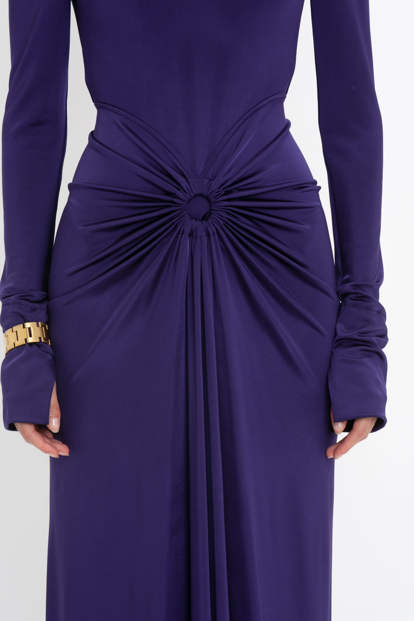 A person wearing a Victoria Beckham Long Sleeve Gathered Midi Dress In Ultraviolet in body-sculpting stretch fabric, with sensuous and playful details at the waist and a gold bracelet on the left wrist.